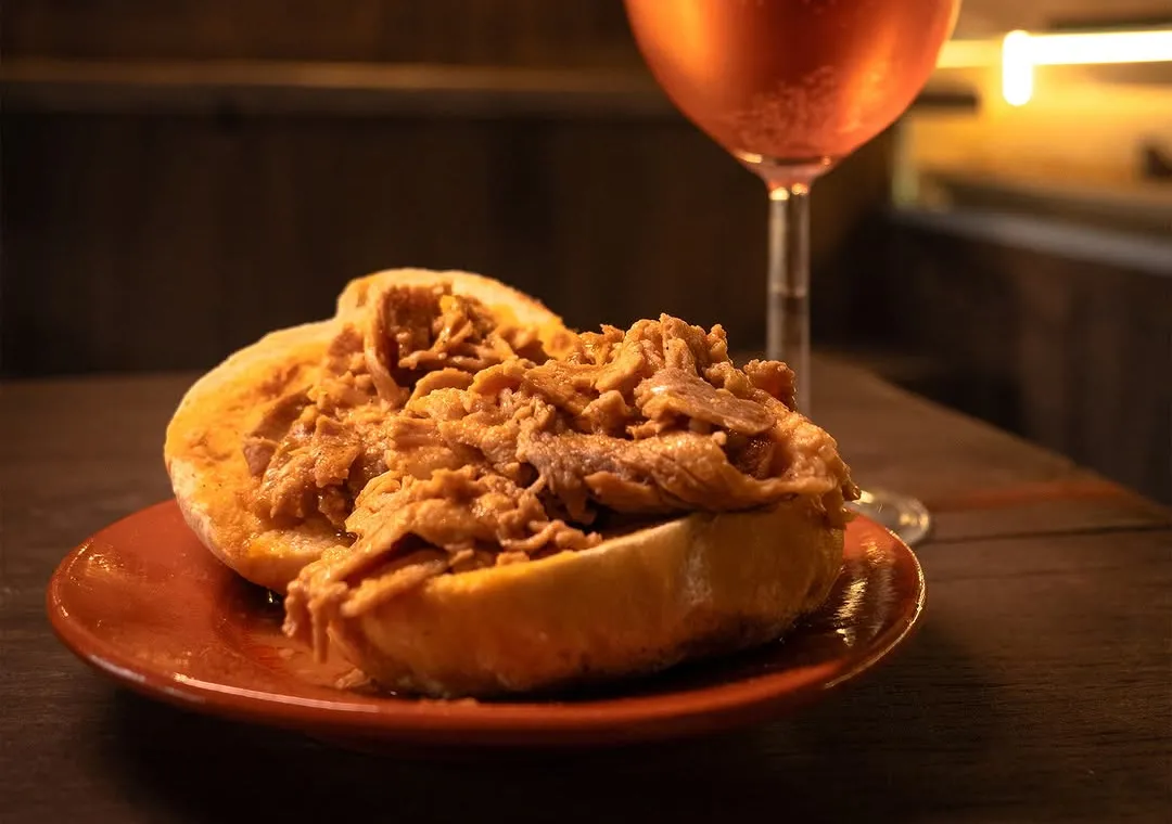 Uma bifana num prato de barro, com um copo de rosé