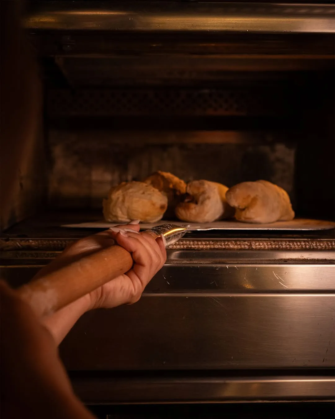 Uma mão põe uma pá de pães no forno